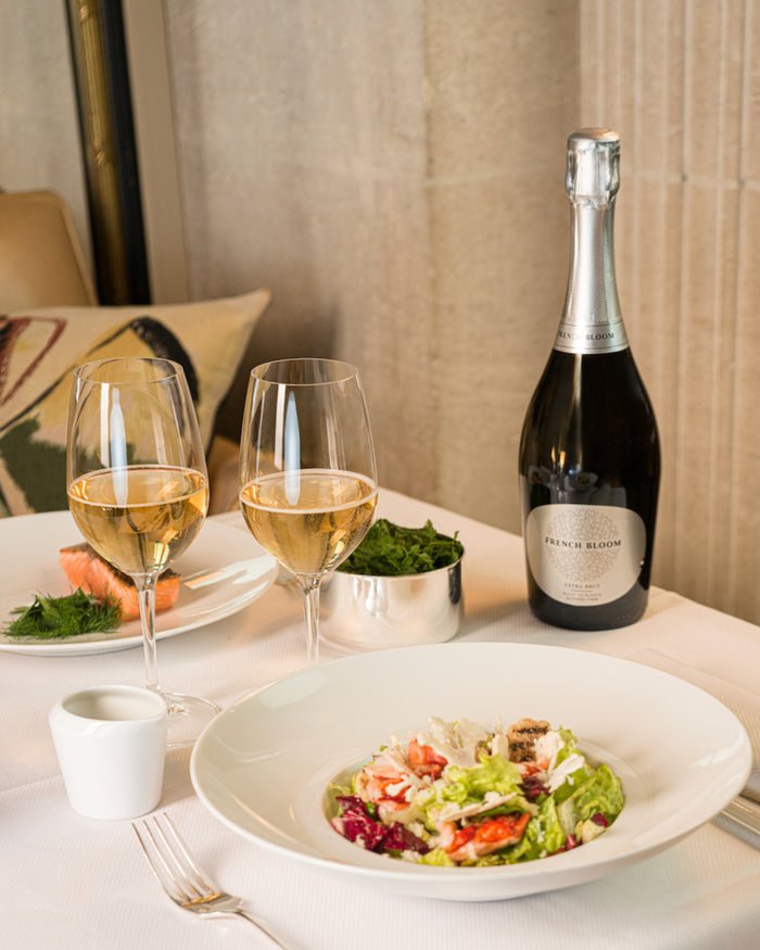 French Bloom Extra Brut non-alcoholic sparkling wine served alongside two glasses and a refined lunch setting.