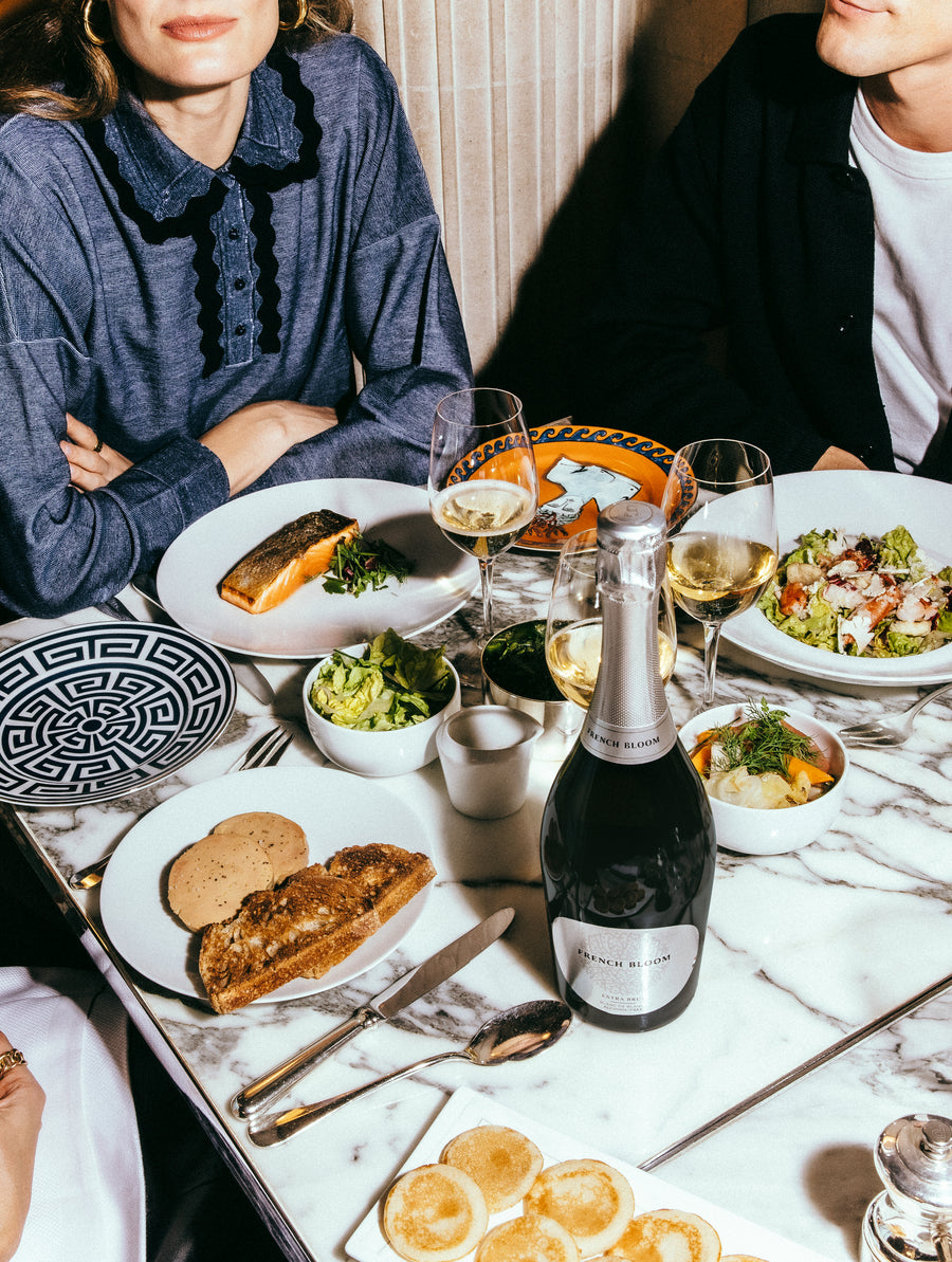 French Bloom L’Extra Brut served with a gourmet meal, surrounded by elegant food pairings and glasses.