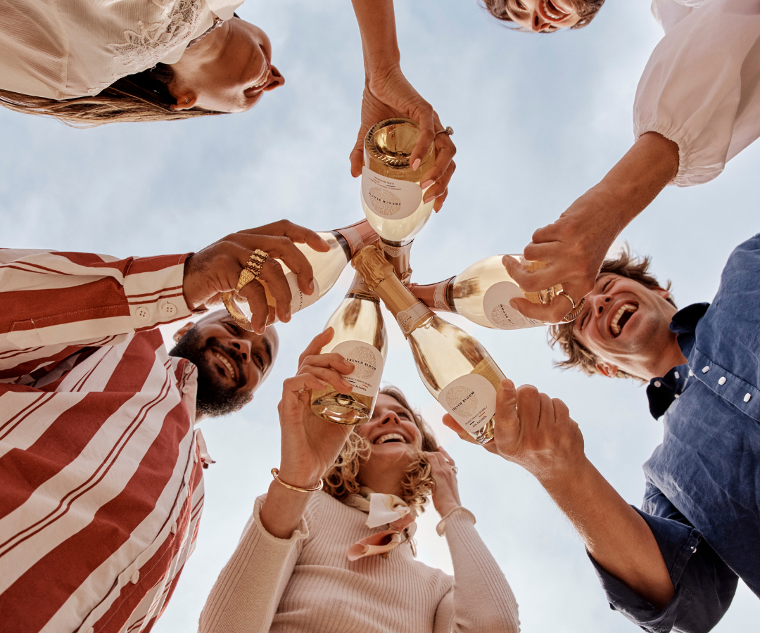 Friends celebrating together with French Bloom half bottles under a bright blue sky.