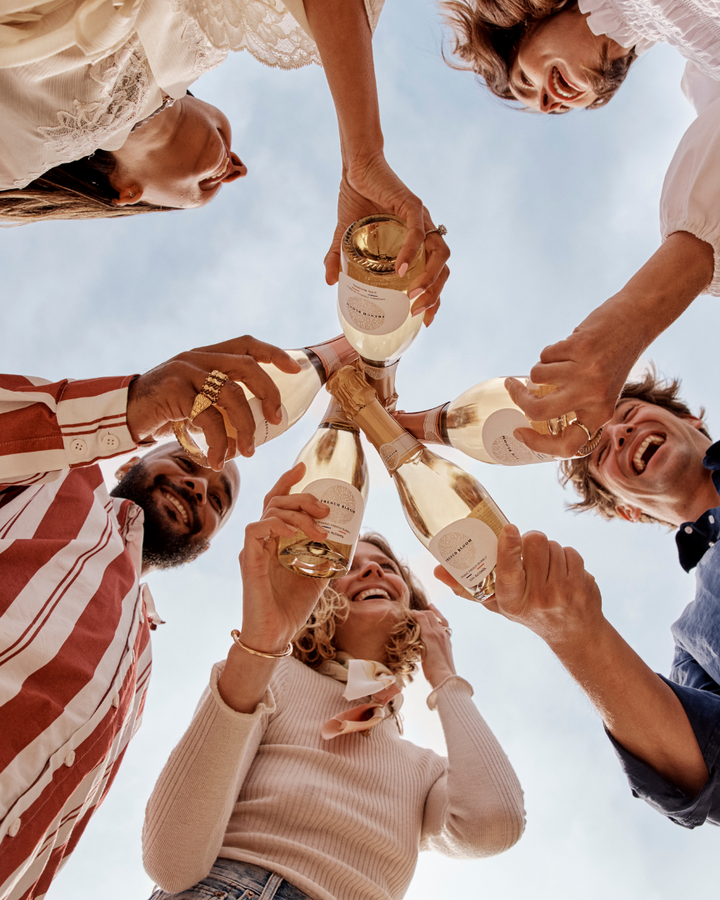 Friends celebrating together with French Bloom half bottles under a bright blue sky.