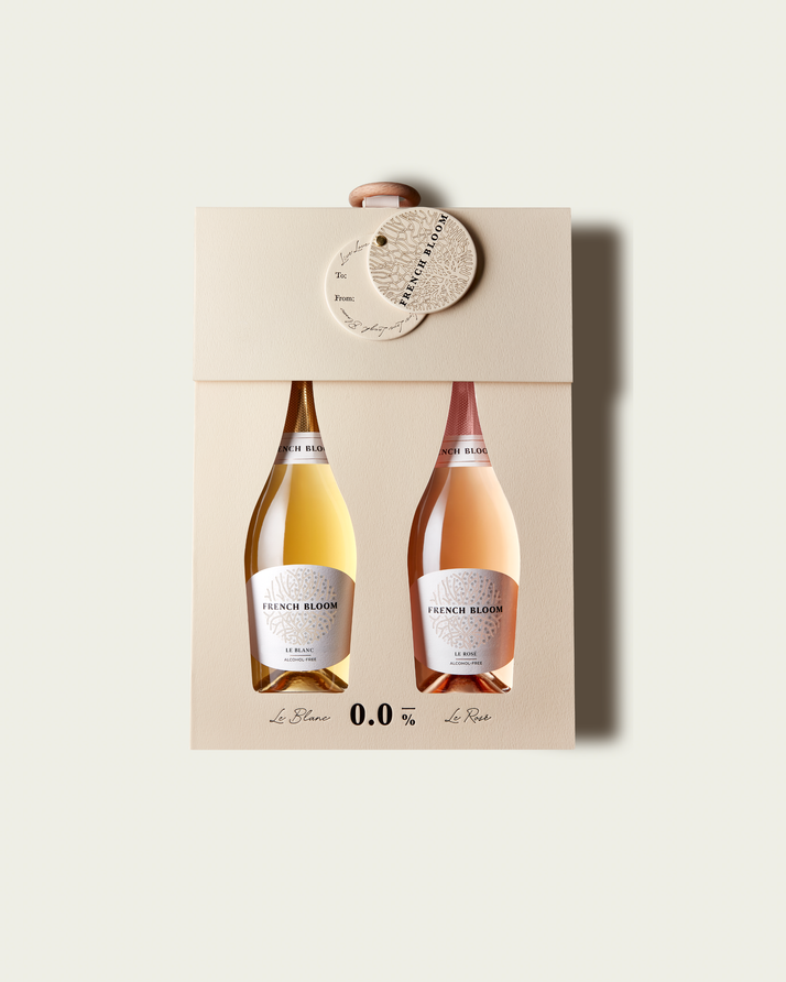 A French Bloom Baby Bloom gift box featuring half bottles of Le Blanc and Le Rosé, with pale golden and pale pink liquid, presented on a light warm-gray background.