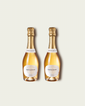 Two half bottles of French Bloom Le Blanc sparkling wine with pale golden liquid and metallic gold foil tops, set against a light warm-gray background.