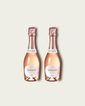 Two half bottles of French Bloom Le Rosé sparkling wine with pale pink liquid and metallic rose-gold foil tops, set against a light warm-gray background.