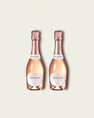 Two half bottles of French Bloom Le Rosé sparkling wine with pale pink liquid and metallic rose-gold foil tops, set against a light warm-gray background.