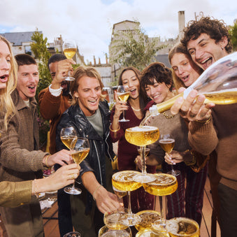 people gathered around a pyramid of non alcoholic champagne glasses, with someone pouring French Bloom into the glasses 