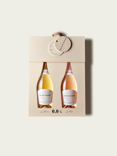 A French Bloom Baby Bloom gift box featuring half bottles of Le Blanc and Le Rosé, with pale golden and pale pink liquid, presented on a light warm-gray background.
