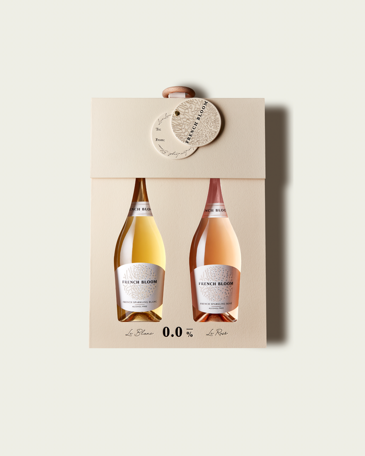 A French Bloom Baby Bloom gift box featuring half bottles of Le Blanc and Le Rosé, with pale golden and pale pink liquid, presented on a light warm-gray background.