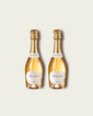 Two half bottles of French Bloom Le Blanc sparkling wine with pale golden liquid and metallic gold foil tops, set against a light warm-gray background.