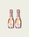 Two half bottles of French Bloom Le Rosé sparkling wine with pale pink liquid and metallic rose-gold foil tops, set against a light warm-gray background.