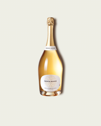 A magnum bottle of French Bloom Le Blanc sparkling wine with pale golden liquid and a metallic gold foil top, set against a light warm-gray background.