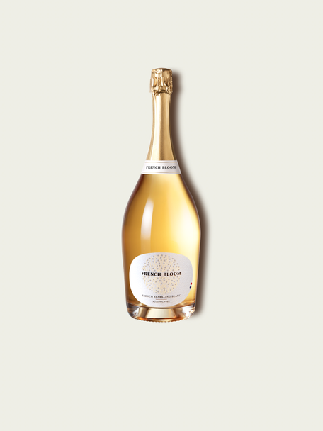 A magnum bottle of French Bloom Le Blanc sparkling wine with pale golden liquid and a metallic gold foil top, set against a light warm-gray background.