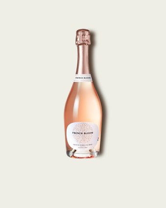 A bottle of French Bloom Le Rosé with pale pink liquid, a white label, and a metallic rose gold foil top, centered on a light beige background.