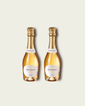 Two half bottles of French Bloom Le Blanc sparkling wine with pale golden liquid and metallic gold foil tops, set against a light warm-gray background.