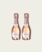 Two half bottles of French Bloom Le Rosé sparkling wine with pale pink liquid and metallic rose-gold foil tops, set against a light warm-gray background.