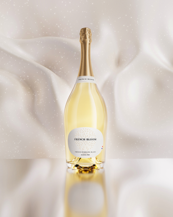 A magnum bottle of French Bloom Le Blanc non-alcoholic sparkling cuvée with pale golden liquid and a metallic gold foil top, set against a softly draped ivory satin background with subtle sparkling details.