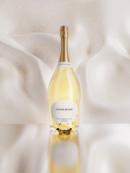 A magnum bottle of French Bloom Le Blanc non-alcoholic sparkling cuvée with pale golden liquid and a metallic gold foil top, set against a softly draped ivory satin background with subtle sparkling details.