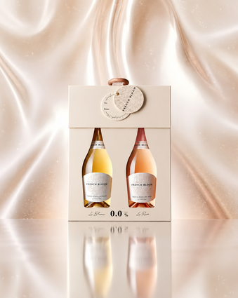 A boxed gift set containing two French Blossom sparkling wine bottles, one white and one rosé, presented in a cream-colored box with a hanging tag, set against a draped champagne-colored fabric background.